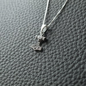 May include: A silver necklace with a detailed silver pendant shaped like a hammer.