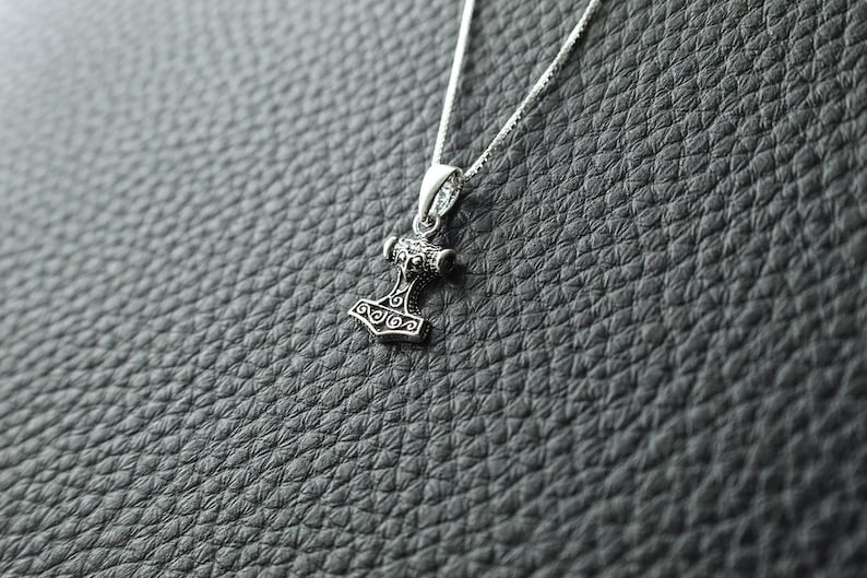 May include: A silver necklace with a detailed silver pendant shaped like a hammer.
