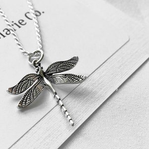 May include: Silver necklace with a detailed dragonfly pendant. The necklace is on a white background with the text "M & Marie Co."