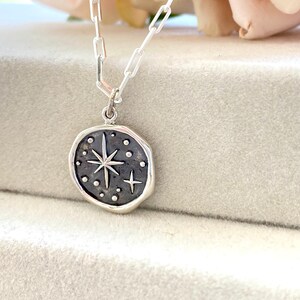 May include: A silver necklace with a round pendant featuring a starburst design with small dots and a smaller star. The pendant is on a silver chain.