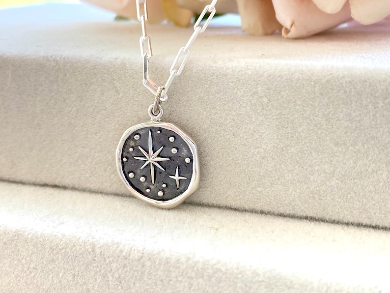 May include: A silver necklace with a round pendant featuring a starburst design with small dots and a smaller star. The pendant is on a silver chain.
