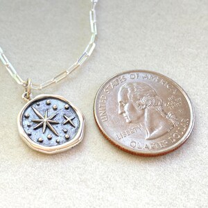May include: A silver chain necklace with a silver pendant featuring a starburst design with smaller stars and dots. The pendant is about the size of a UK 20 pence coin.