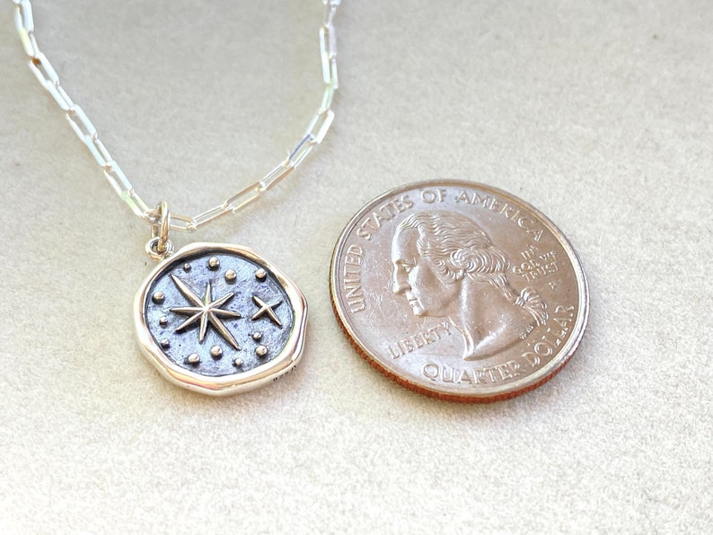 May include: A silver chain necklace with a silver pendant featuring a starburst design with smaller stars and dots. The pendant is about the size of a UK 20 pence coin.