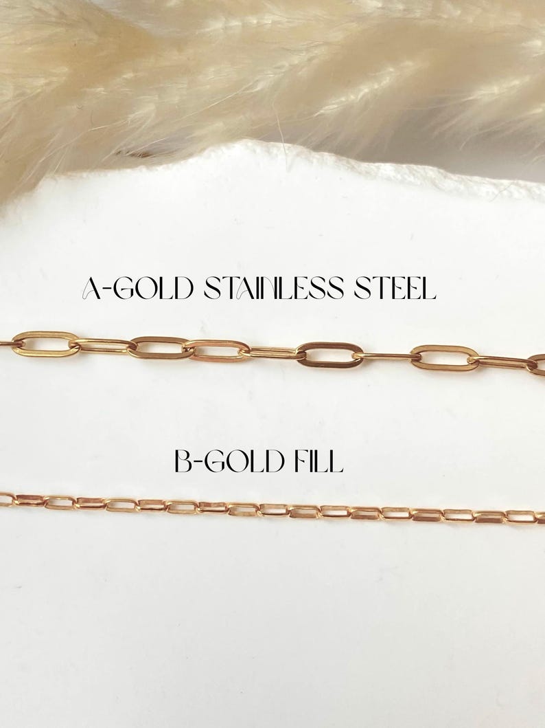 May include: Two gold-colored chain necklaces are displayed against a white background. The top chain is labeled "A-GOLD STAINLESS STEEL" and features large oval links. The bottom chain, labeled "B-GOLD FILL", has smaller rectangular links. The chains are presented in a jewelry product shot.