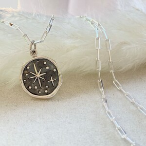 May include: A silver necklace with a round pendant featuring a starburst design with small dots around it.