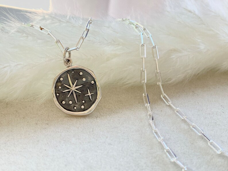 May include: A silver necklace with a round pendant featuring a starburst design with small dots around it.