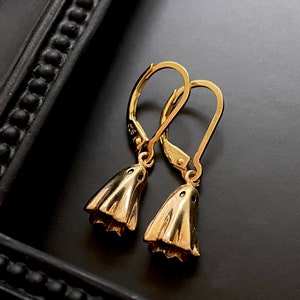 May include: A pair of gold dangle earrings with a bell-shaped design. The earrings have a simple, elegant style.