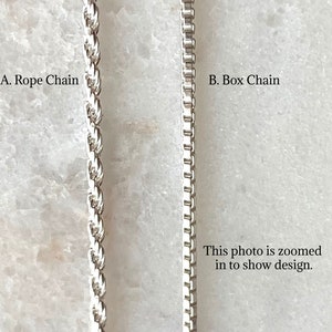 May include: Close-up of two silver chains, a rope chain and a box chain. The photo is zoomed in to show the design.