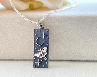 May include: A silver necklace with a rectangular pendant featuring a crescent moon, stars, and a moth design.