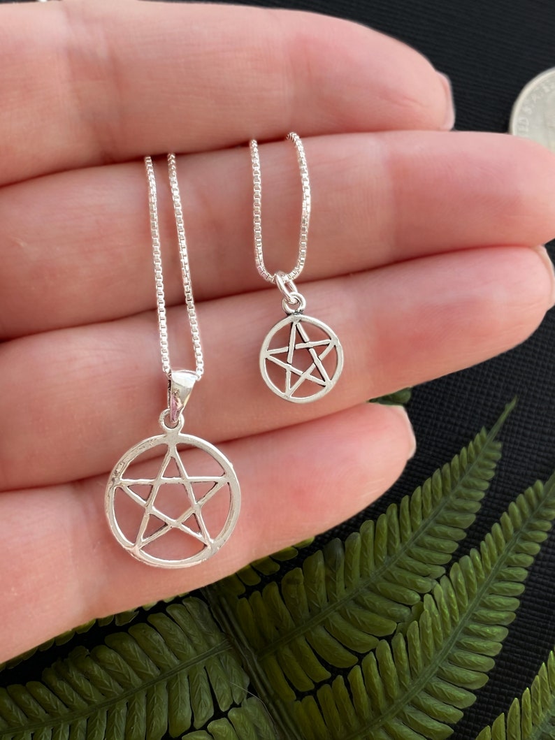 May include: Two silver necklaces with pentacle pendants. The necklaces are on a chain and the pendants are different sizes.