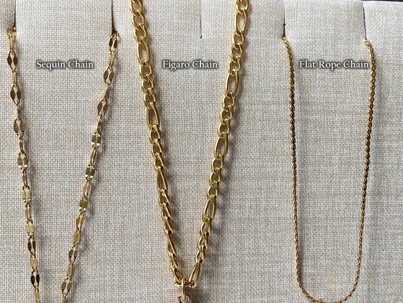 Peut inclure: Gros plan de quatre cha&icirc;nes en or sur un fond en tissu beige. Les cha&icirc;nes sont &eacute;tiquet&eacute;es "Sequin Chain", "Figaro Chain", "Flat Rope Chain".