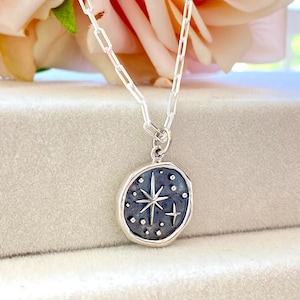 May include: A silver chain necklace with a silver pendant featuring a star with a small cross on a dark blue background.