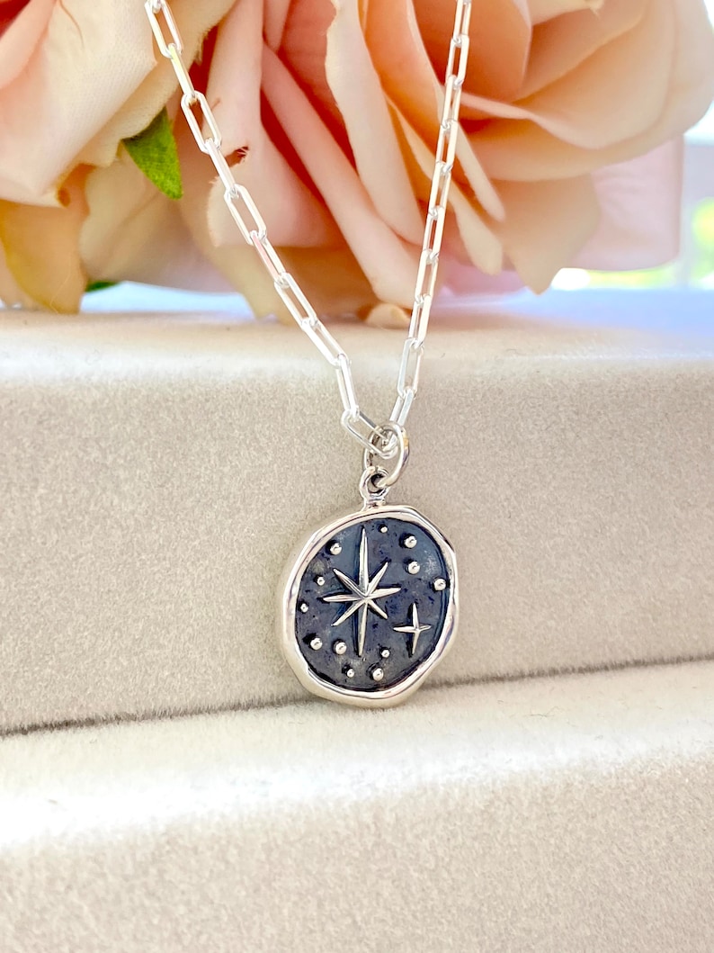 May include: A silver chain necklace with a silver pendant featuring a star with a small cross on a dark blue background.