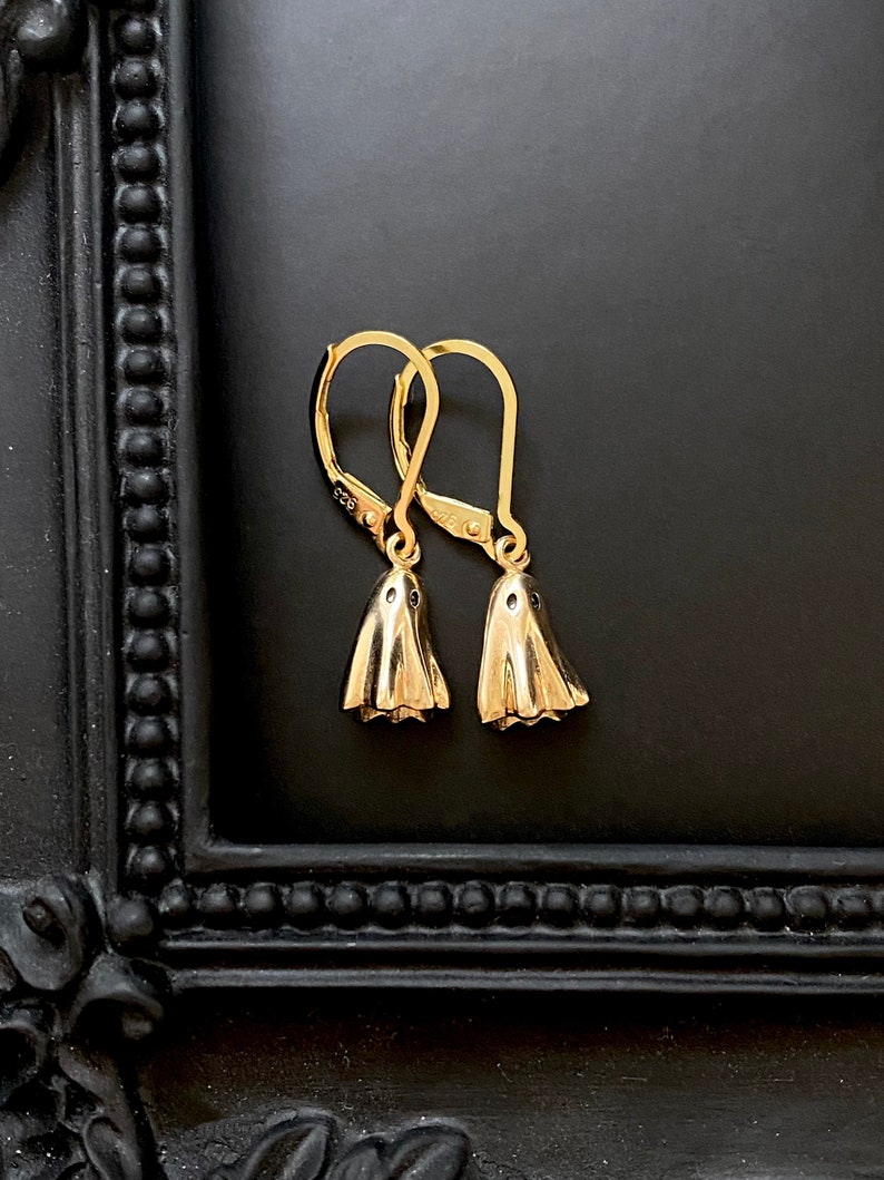 May include: A pair of gold-tone ghost-shaped dangle earrings with black accents. The earrings have a hook closure.