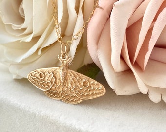 Peut inclure: Un collier en chaîne dorée avec un pendentif en forme de papillon de nuit doré texturé et détaillé. Le pendentif est une représentation réaliste d'un papillon de nuit avec des motifs d'ailes complexes.
