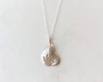 May include: A silver necklace with a delicate chain and a pendant shaped like an oyster shell.