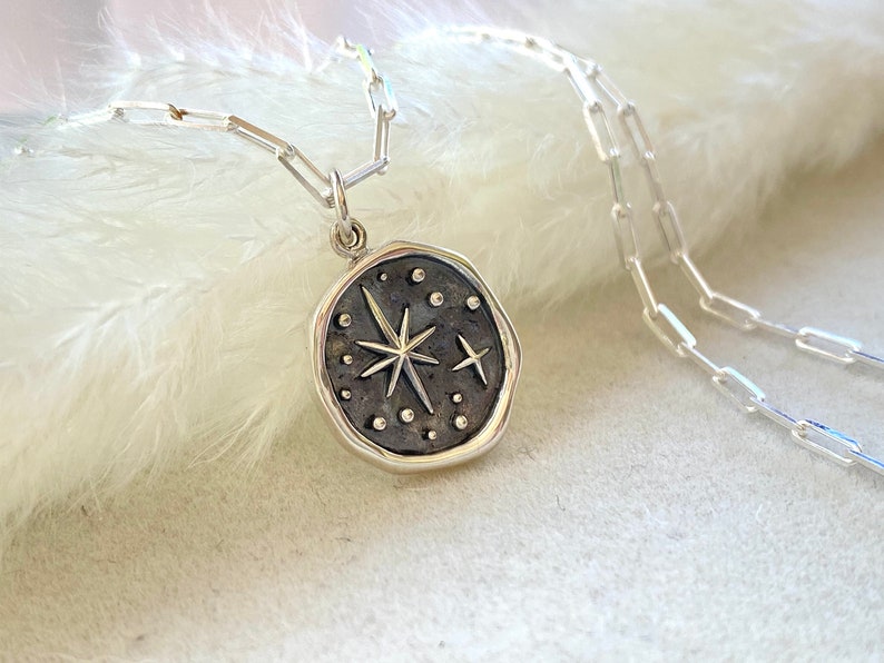 May include: A silver chain necklace with a silver pendant featuring a starburst design with small dots around it.