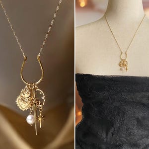 May include: Gold-toned necklace with a U-shaped pendant and multiple charms. Charms include a heart, sword, star, and pearl. The necklace is displayed on a mannequin with a black lace top.