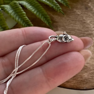 May include: A silver chain necklace with a small silver mouse charm. The chain is box style and the mouse is facing to the right.