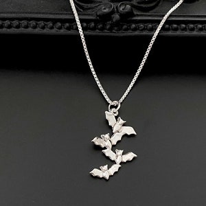 May include: A silver necklace with a pendant of five bats clustered together. The bats are all facing the same direction and are arranged in a cascading pattern.