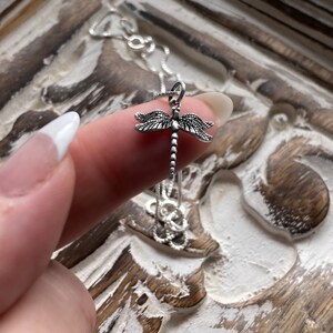 May include: A silver chain necklace with a dragonfly pendant. The dragonfly is detailed with intricate wings and a long, thin body.