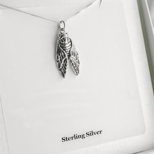 May include: A silver necklace with a detailed cicada pendant. The pendant is made of sterling silver and has a delicate, intricate design. The necklace is displayed on a white background with the words "Sterling Silver" printed below the pendant.