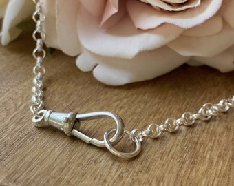 May include: A silver chain with a silver clasp. The chain is on a wooden surface with a pink rose in the background.