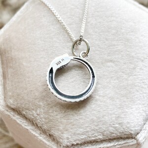 May include: A silver snake necklace with a circular pendant. The pendant has a black enamel finish and the words "925 N" are engraved on the back.