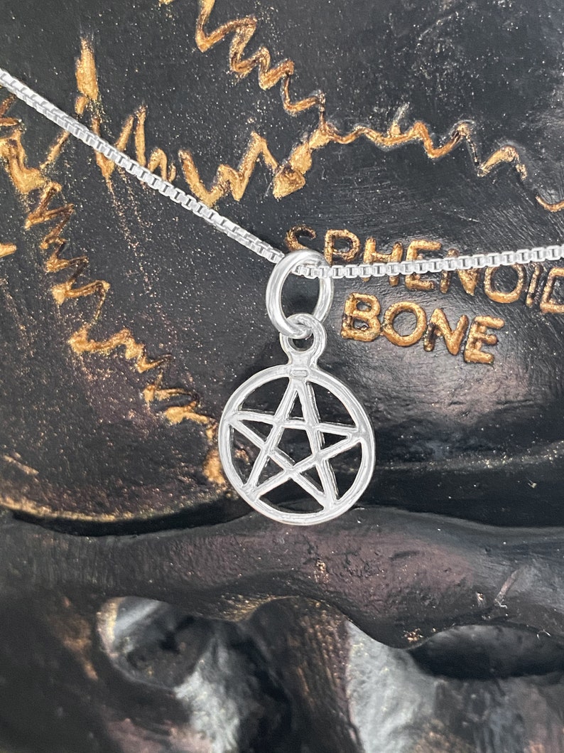 May include: A silver chain necklace with a silver pentagram pendant. The pendant is a five-pointed star with a circle around it. The necklace is on a black background with gold writing.