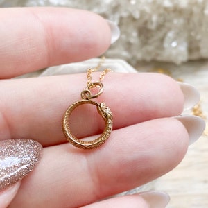 May include: A gold snake necklace with a coiled snake pendant. The snake's head is facing the viewer and its tail is curled around the pendant.
