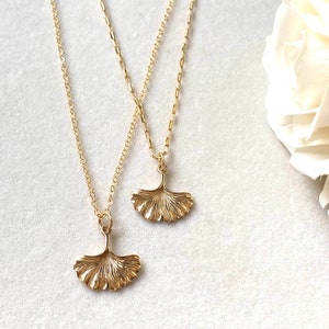 May include: Two gold necklaces with ginkgo leaf pendants. The necklaces are layered and the leaves are detailed.