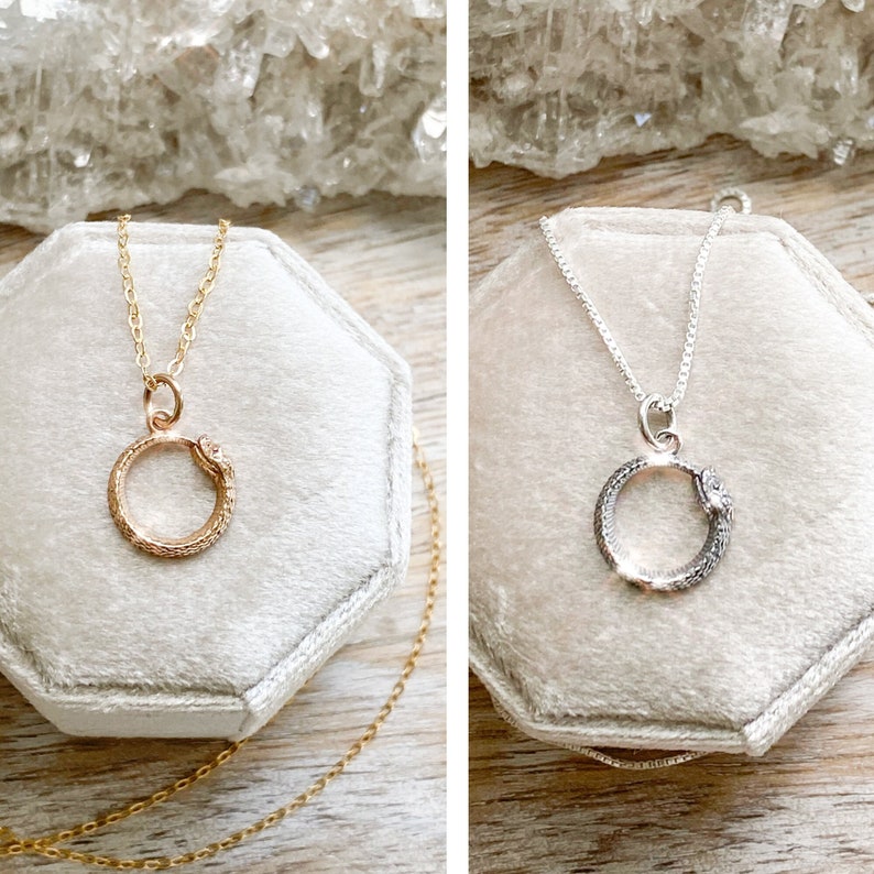 May include: Two delicate snake necklaces, one in gold and one in silver, are displayed in velvet boxes. The snake is curled in a circle, with its tail in its mouth, symbolizing eternity.