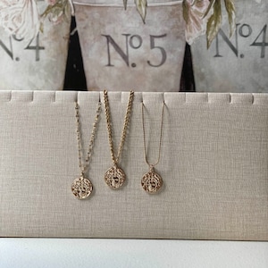 Peut inclure: Trois colliers en or avec des pendentifs ronds pr&eacute;sentant un design d&eacute;taill&eacute;. Les colliers sont pr&eacute;sent&eacute;s sur un fond en tissu beige.