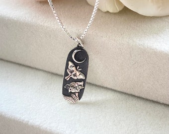 May include: A silver chain necklace with a pendant featuring a crescent moon, two moths, and a floral design. The pendant is oval-shaped and has a dark oxidized finish.