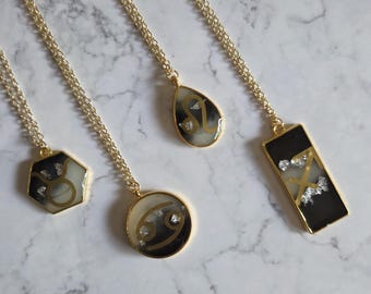 May include: Four gold-tone chain necklaces featuring resin pendants in various shapes including a hexagon, circle, teardrop, and rectangle. Each pendant contains a black and white marbled background with gold zodiac symbols and silver foil accents.