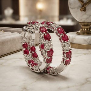 May include: A pair of hoop earrings crafted from silver-toned metal, featuring an alternating pattern of round-cut vibrant red gemstones and clear white stones set in a continuous circular design with a secure hinged closure mechanism.