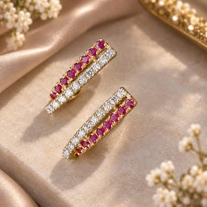 Puede incluir: Un par de pendientes de oro con un diseño de doble fila. Una fila está engastada con rubíes rojos redondos y vibrantes, mientras que la fila adyacente tiene diamantes blancos claros y brillantes. Los pendientes tienen una forma de barra alargada.