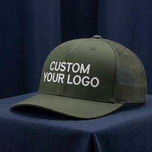 May include: An olive green baseball cap featuring a structured front panel and a mesh back. The front of the cap displays the white embroidered text CUSTOM YOUR LOGO in a bold, sans-serif font. The cap has a curved brim and a matching olive green button.