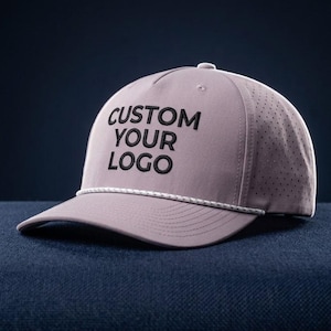 Puede incluir: Una gorra de béisbol de color malva claro con un detalle de cuerda blanca en la base de la corona y texto bordado en negro que dice CUSTOM YOUR LOGO. Los paneles laterales de la gorra están hechos con un material perforado para ventilación.