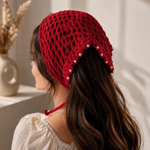 May include: A deep red crochet headscarf featuring an openwork diamond pattern and a scalloped edge adorned with small white faux pearls. The triangular head covering includes thin matching red ties at the base to secure it in place.