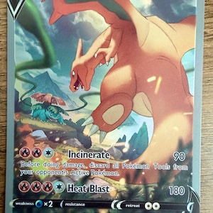 May include: A Charizard V trading card with 220 HP, featuring a large orange dragon-like creature flying above a smaller green Venusaur. The card displays the attacks Incinerate and Heat Blast, along with game rules, set number 154/172, and 2022 copyright.