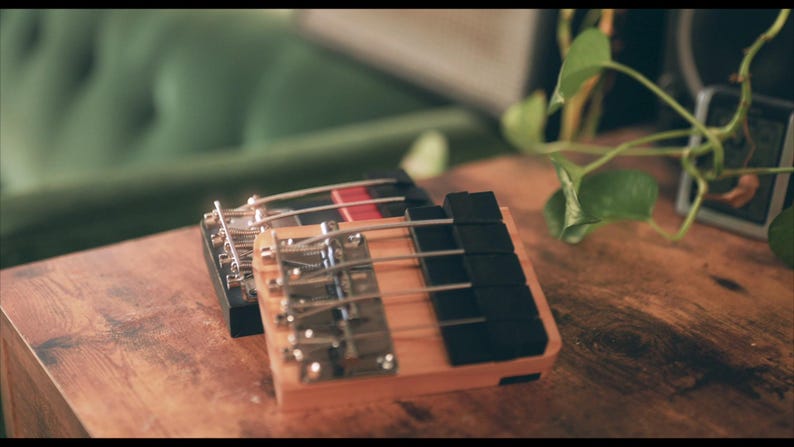 May include: Two rectangular wooden musical instruments with metal tines and black keys. The front instrument features a light wood base, while the rear instrument has a dark wood base with a red accent. Both have silver metal hardware components.