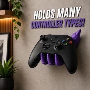May include: A purple wall-mounted controller holder shaped like a clawed hand, securely gripping a black wireless gaming controller. The text HOLDS MANY CONTROLLER TYPES! is displayed in white and purple lettering above the mount on the wall.