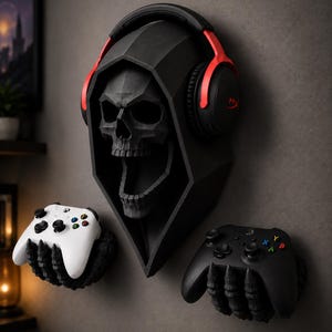 May include: A black geometric wall-mounted skull wearing black and red over-ear headphones, accompanied by two black skeletal hand wall mounts, one holding a white game controller and the other holding a black game controller.