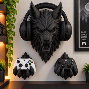 Könnte beinhalten: Eine schwarze Wandskulptur in Form eines Wolfskopfes mit schwarzem Kopfhörer, platziert über zwei klauenförmigen Wandhalterungen, die links einen weißen und rechts einen schwarzen Gamecontroller halten, ergänzt durch ein gerahmtes Poster.