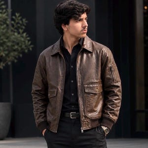 Brown leather bomber jacket with zip front, multiple flap pockets, ribbed cuffs, and sleeve pocket, worn by a male model against a stylish background