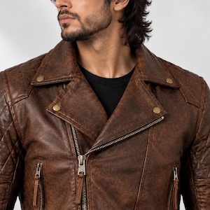 Pu&ograve; includere: Una giacca da moto in pelle marrone con finitura invecchiata, pannelli trapuntati sulle spalle, ampio bavero con bottoni a pressione metallici e chiusura frontale con zip diagonale dotata di linguette in pelle sulle tasche laterali.