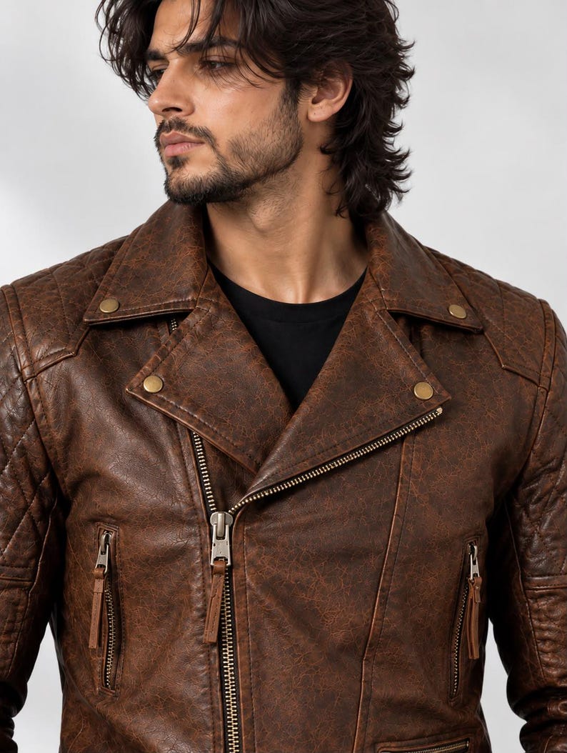 Pu&ograve; includere: Una giacca da moto in pelle marrone con finitura invecchiata, pannelli trapuntati sulle spalle, ampio bavero con bottoni a pressione metallici e chiusura frontale con zip diagonale dotata di linguette in pelle sulle tasche laterali.
