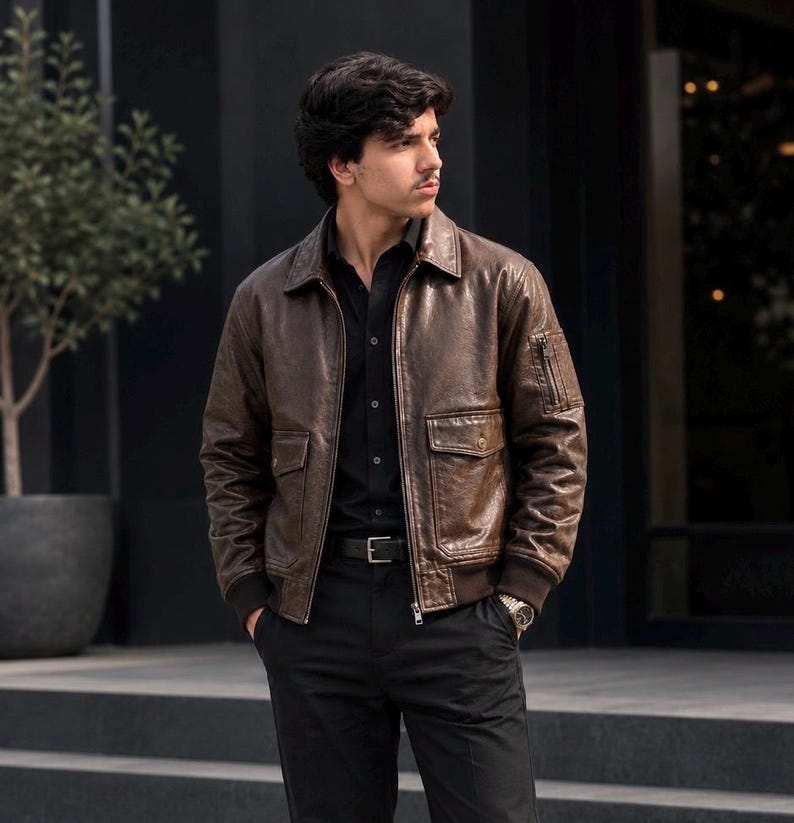 Brown leather bomber jacket with zip front, multiple flap pockets, ribbed cuffs, and sleeve pocket, worn by a male model against a stylish background