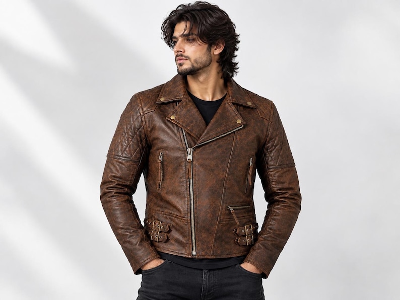 A brown leather motorcycle jacket featuring a distressed finish, an asymmetrical front zip, quilted shoulder panels, notched lapels with metallic snap buttons, two zipped chest pockets, and adjustable side buckles at the waist.
